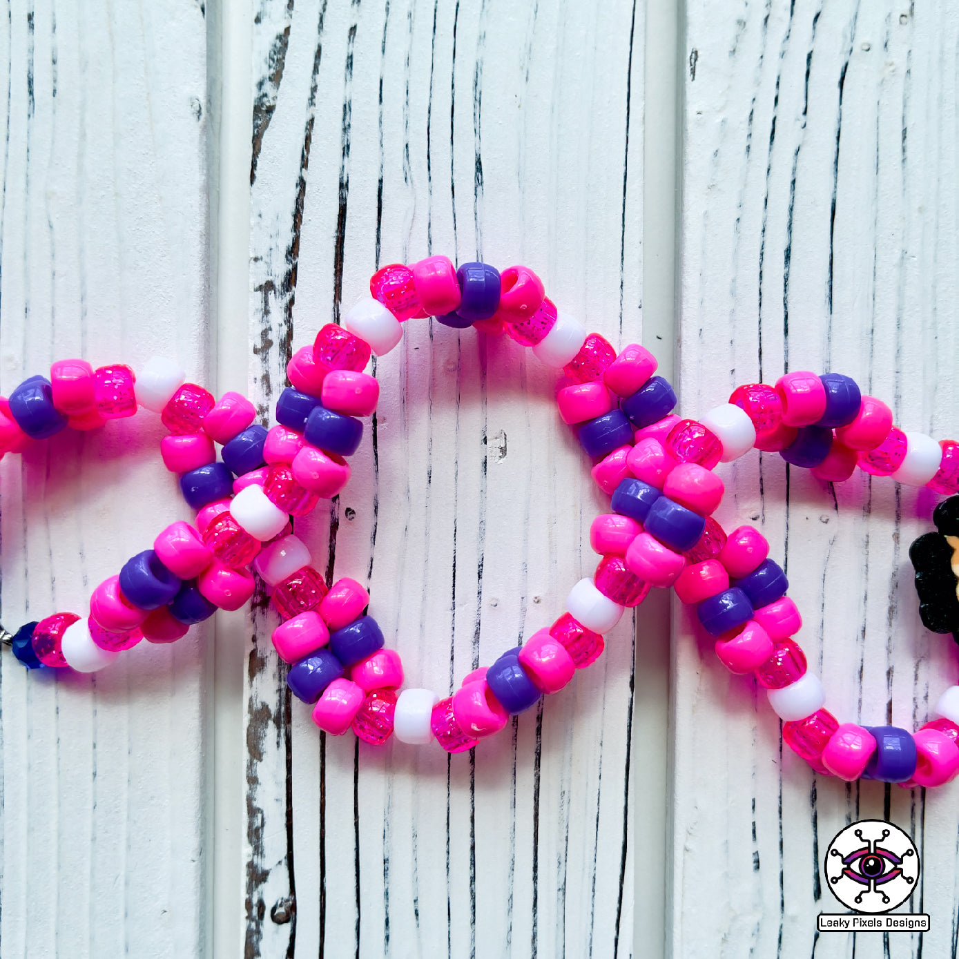 bottle in the shape of a heart that has a label on it that says Boys Tears made by Leaky Pixels. It is filled with a pink liquid. pink and purple perler necklace.