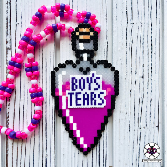 bottle in the shape of a heart that has a label on it that says Boys Tears made by Leaky Pixels. It is filled with a pink liquid. pink and purple perler necklace.