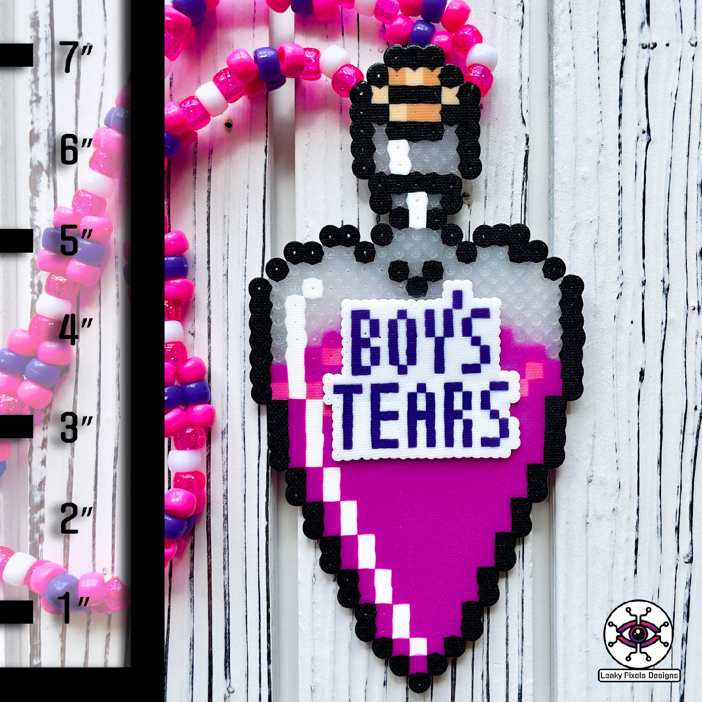bottle in the shape of a heart that has a label on it that says Boys Tears made by Leaky Pixels. It is filled with a pink liquid. pink and purple perler necklace.