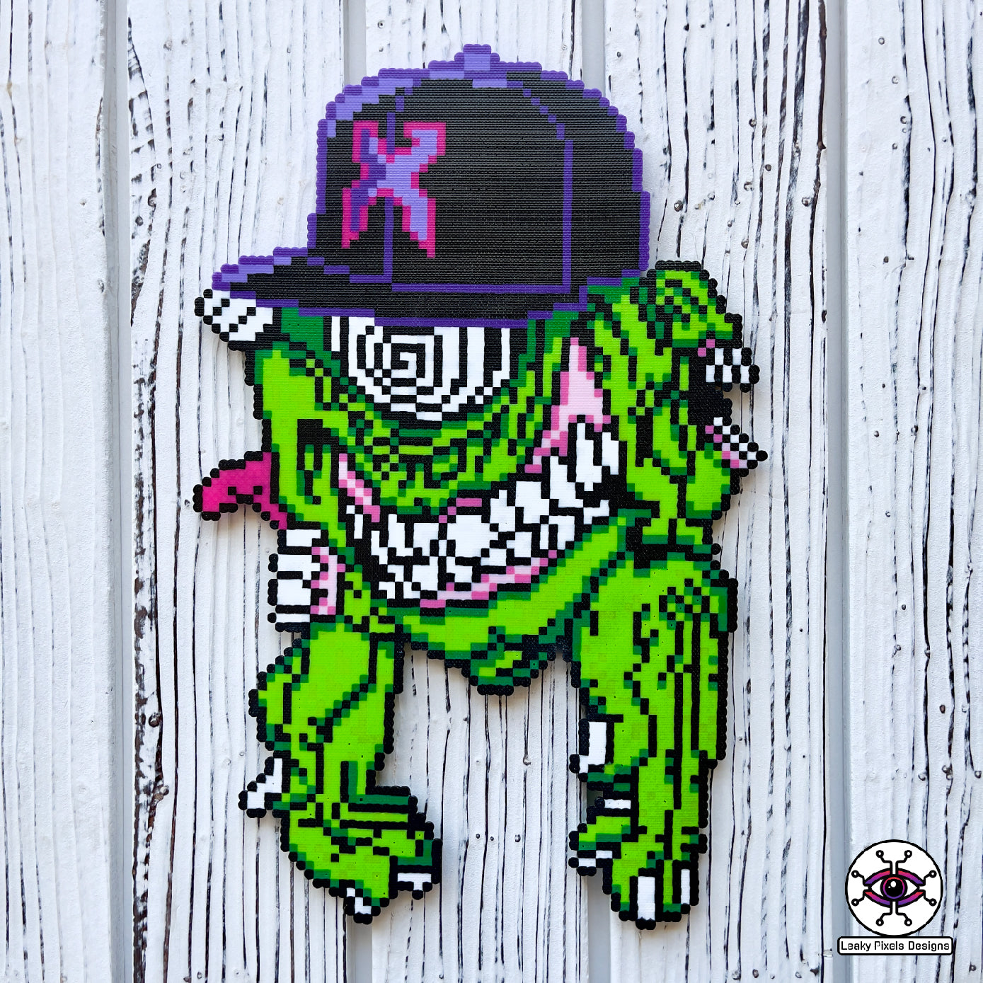 Excision Subtronics Cyclops Perler Necklace Green. One eyed green cyclops monster with hypnotizing rezz spiral eye. Two mouths are on each side of its head one with its tongue sticking out. big grin on its face bearing teeth and long hands below him.