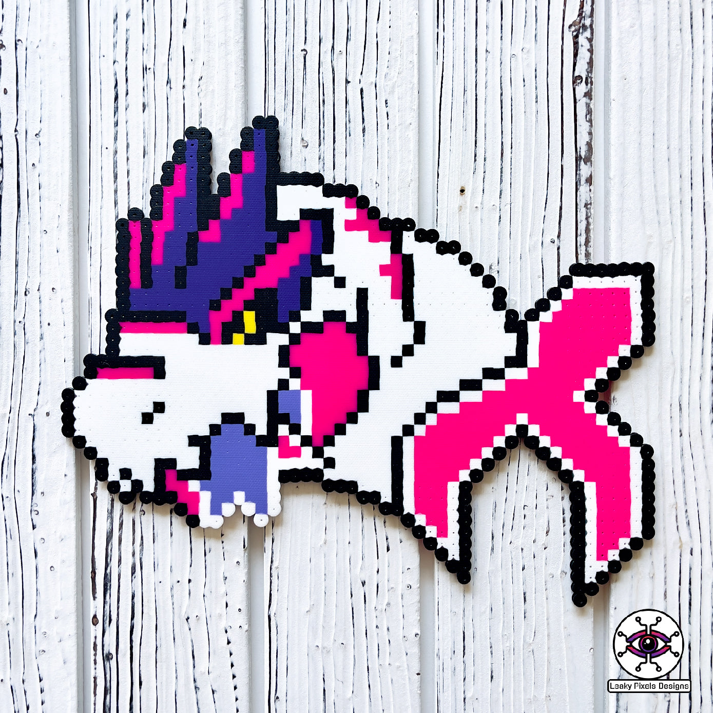 Pink and white trex perler necklace made by leaky pixels. the trex is bursting through the excision x with a piece in its mouth.
