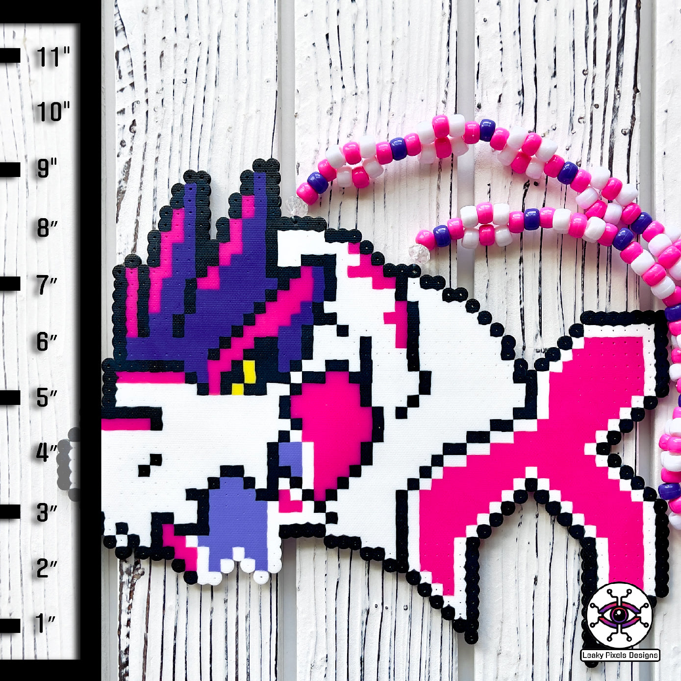 Pink and white trex perler necklace made by leaky pixels. the trex is bursting through the excision x with a piece in its mouth.