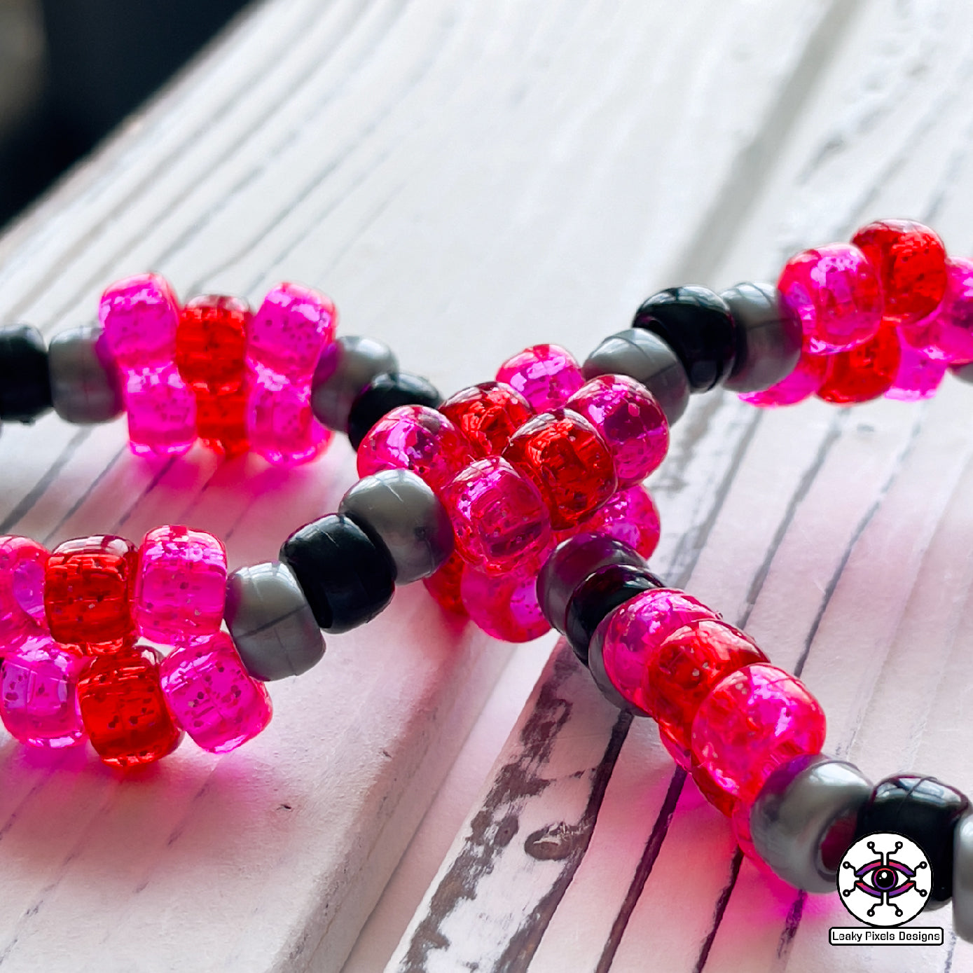galarian moltres pokemon perler necklace made by leaky pixles. megenta, pink and red legendary bird with fire wings. dark grey body.pink and red glitter pony beads make up the necklace.