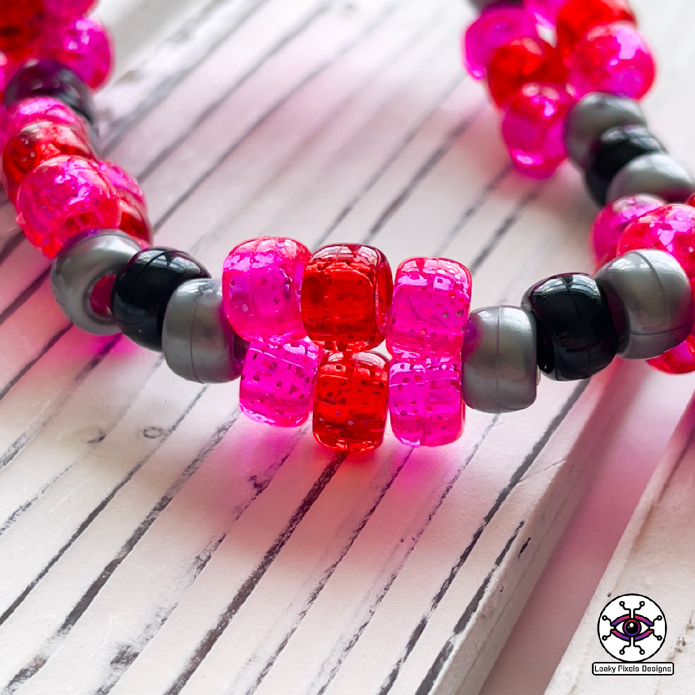 galarian moltres pokemon perler necklace made by leaky pixles. megenta, pink and red legendary bird with fire wings. dark grey body.pink and red glitter pony beads make up the necklace.