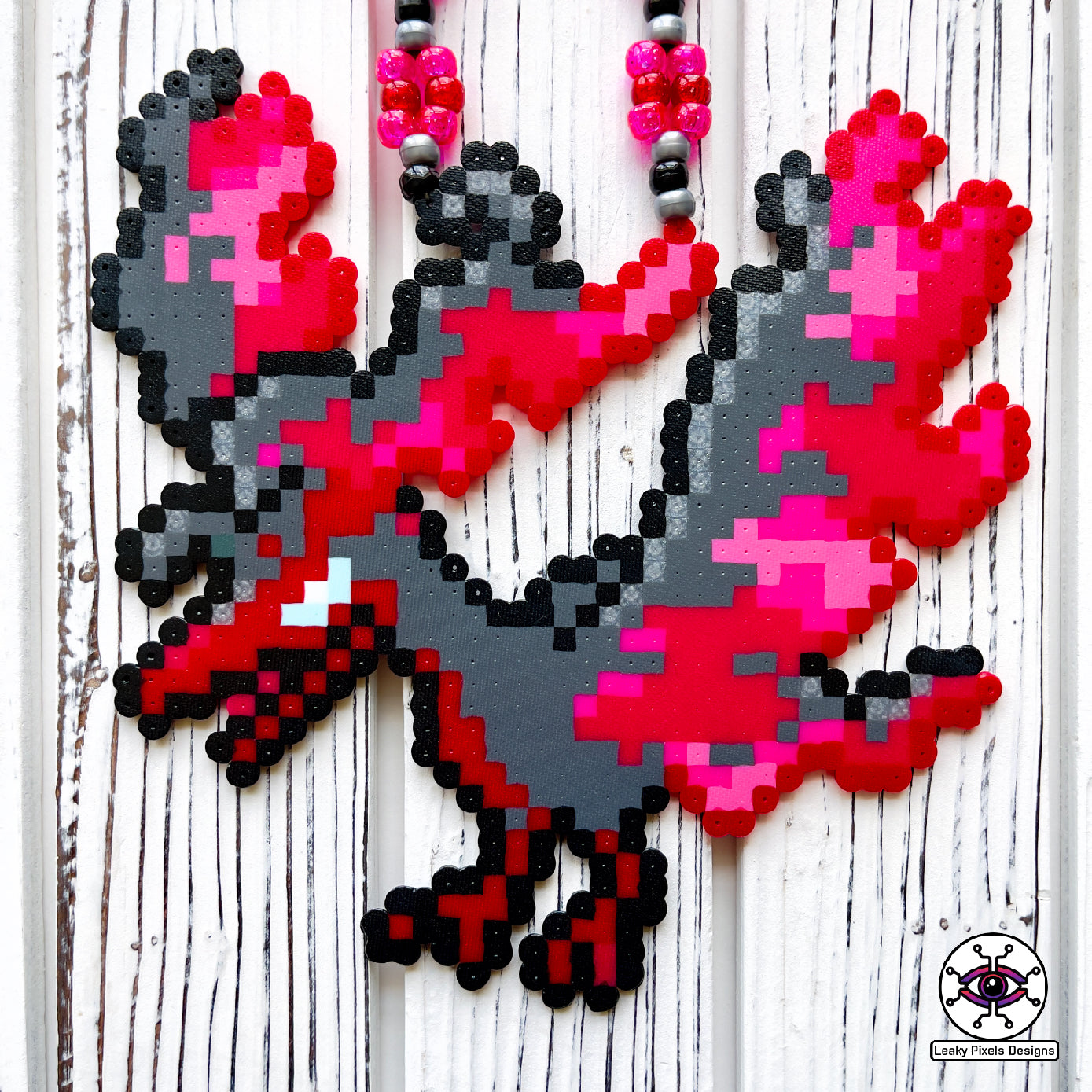 galarian moltres pokemon perler necklace made by leaky pixles. megenta, pink and red legendary bird with fire wings. dark grey body.pink and red glitter pony beads make up the necklace.