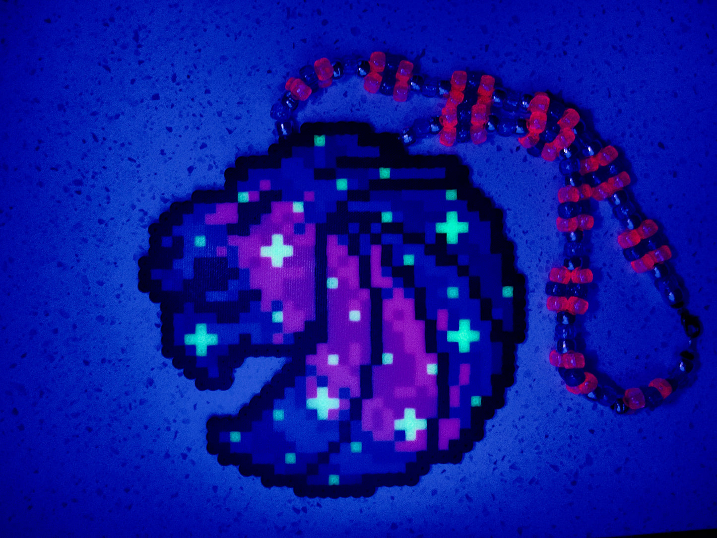 Seven Lions galaxy perler necklace. seven lions logo made of purple, pink, teal, blue and white starts. image of a galaxy. necklace is made of purple, blue, and pink pearl pony beads.