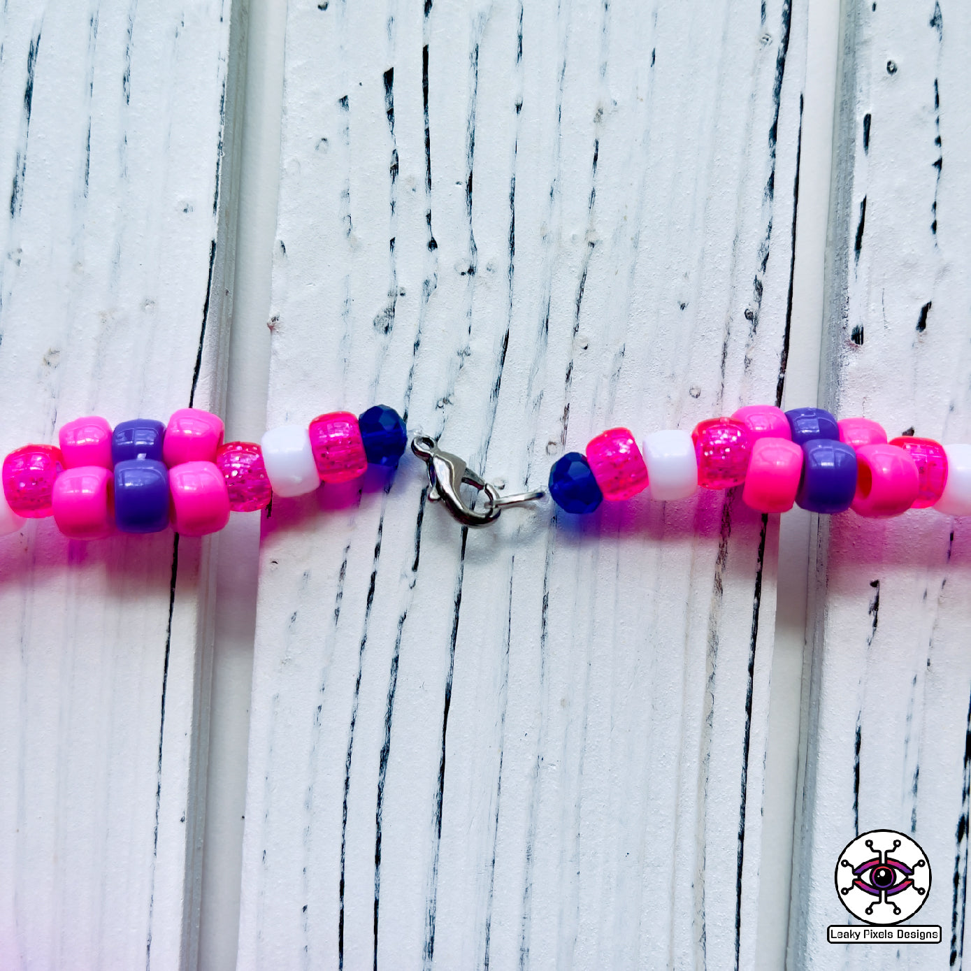 bottle in the shape of a heart that has a label on it that says Boys Tears made by Leaky Pixels. It is filled with a pink liquid. pink and purple perler necklace.