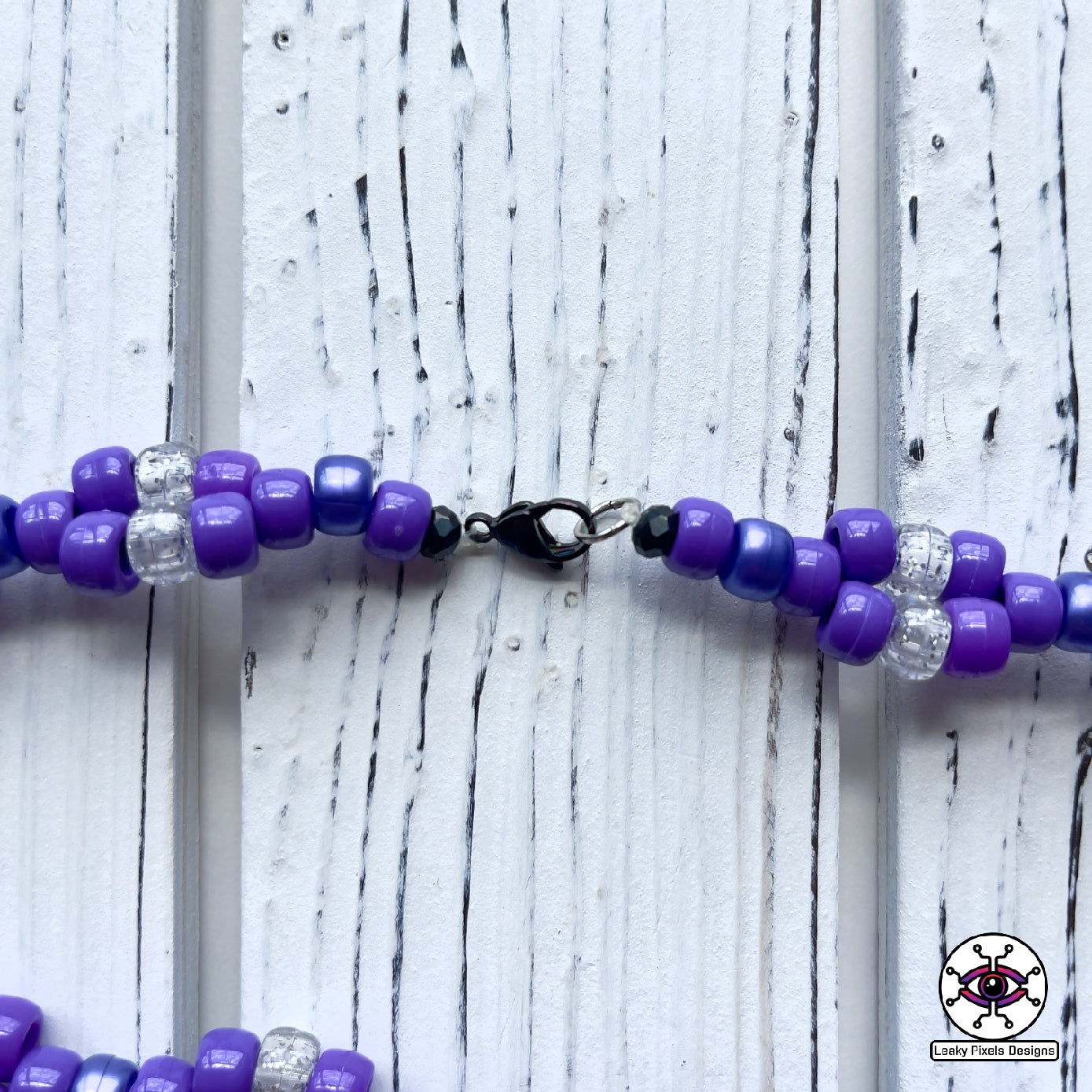 Espion perler necklace. Perler of the pokemon Espion that is cat like with fur colors of lavender and purple. Has a red gem stone on her forehead. Pony beads are purple for the necklace.
