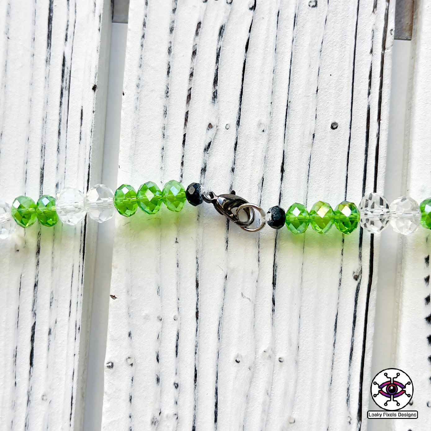 Excision Subtronics Cyclops Perler Necklace Green. One eyed green cyclops monster with hypnotizing rezz spiral eye. Two mouths are on each side of its head one with its tongue sticking out. big grin on its face bearing teeth and long hands below him.