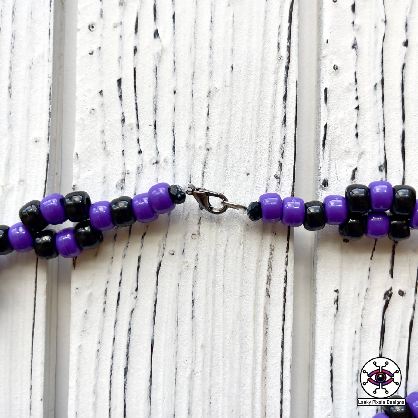 Haunter pokemon perler necklace. black and purple ghost with hot coral glowing hands. necklace is made of purple and black glitter pony beads on a nice wood background.