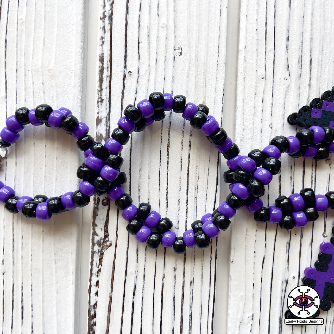 Haunter pokemon perler necklace. black and purple ghost with hot coral glowing hands. necklace is made of purple and black glitter pony beads on a nice wood background.