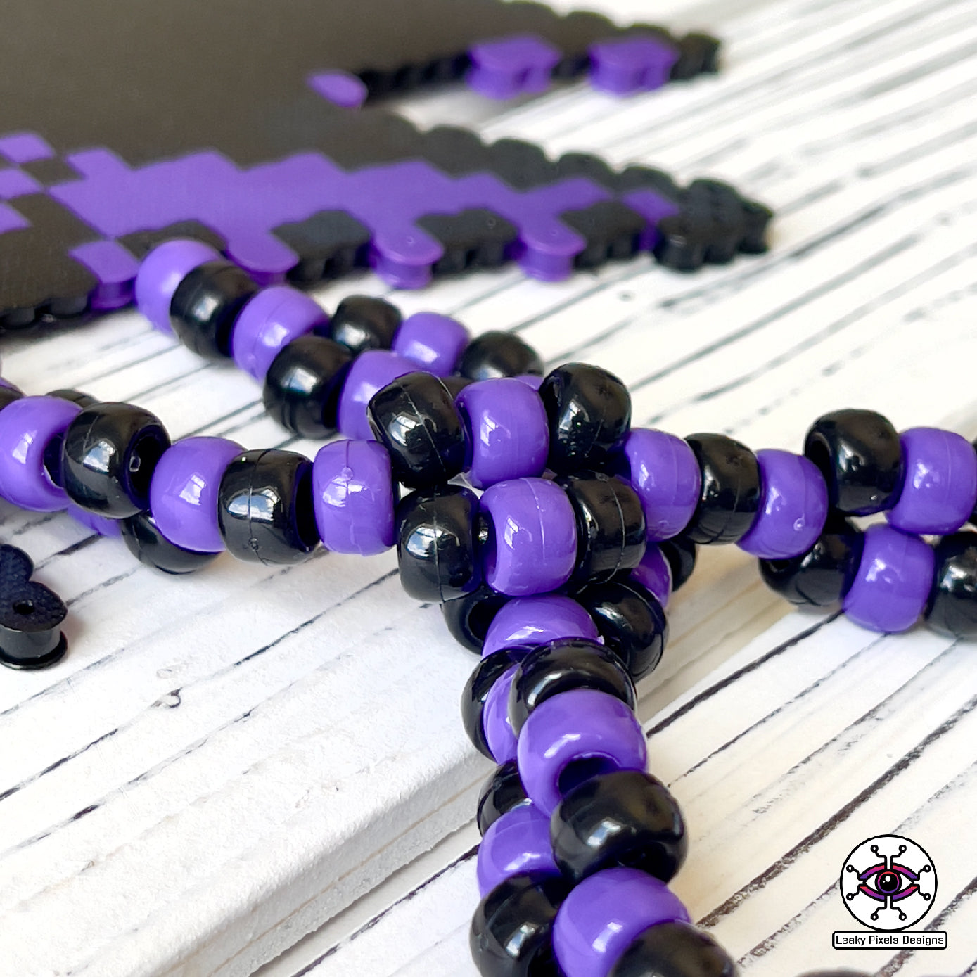 Haunter pokemon perler necklace. black and purple ghost with hot coral glowing hands. necklace is made of purple and black glitter pony beads on a nice wood background.