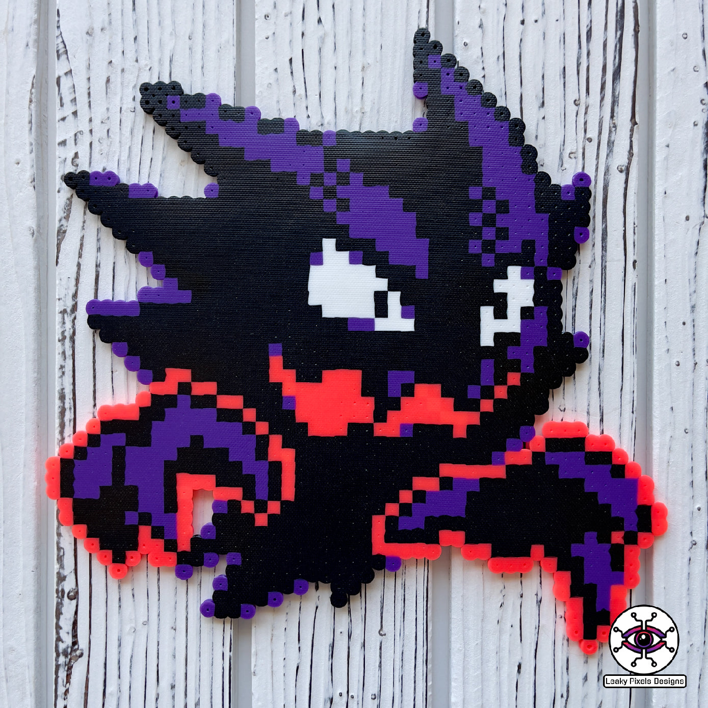 Haunter pokemon perler necklace. black and purple ghost with hot coral glowing hands. necklace is made of purple and black glitter pony beads on a nice wood background.