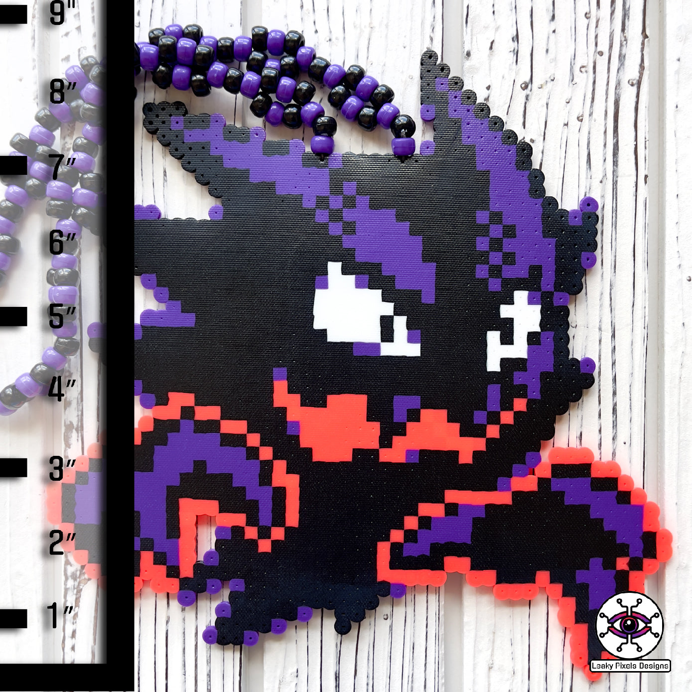 Haunter pokemon perler necklace. black and purple ghost with hot coral glowing hands. necklace is made of purple and black glitter pony beads on a nice wood background.