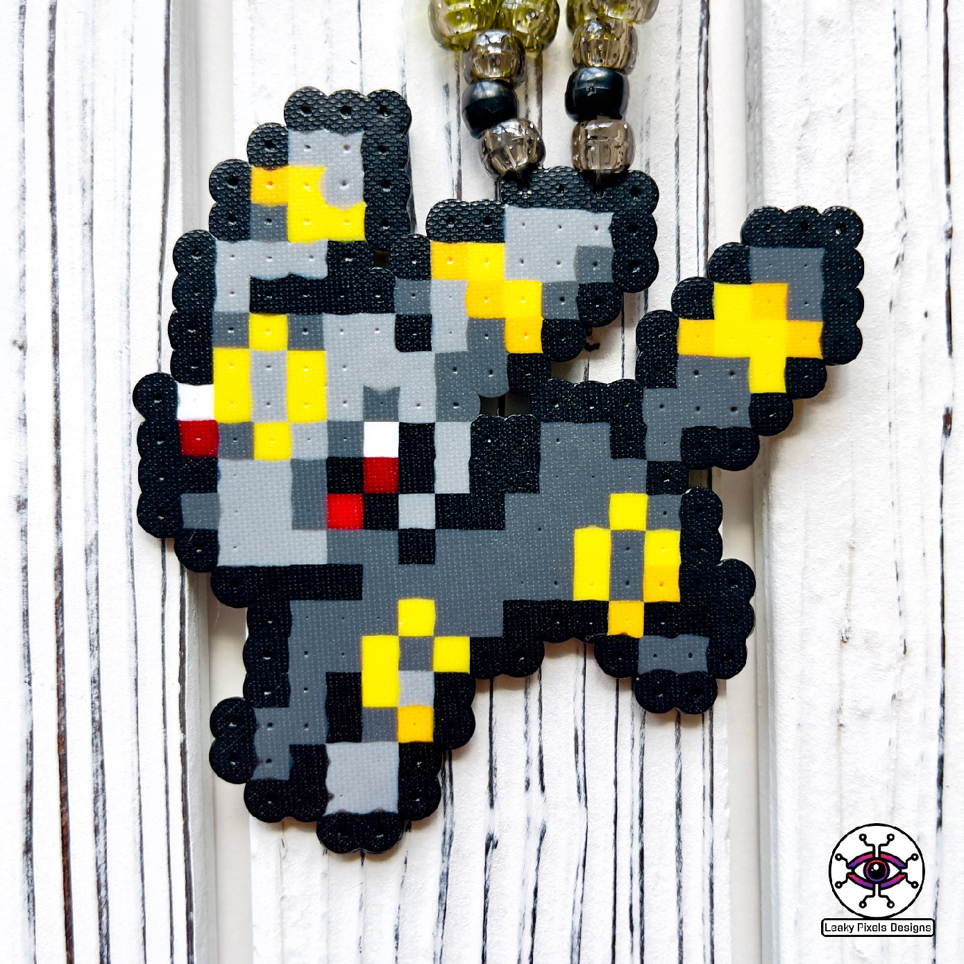 Umbreon pokemon perler necklace. eevee evolution. dark grey with red eyes and gold rings on its body. necklace is made of clear, black, and yellow glitter pony beads.
