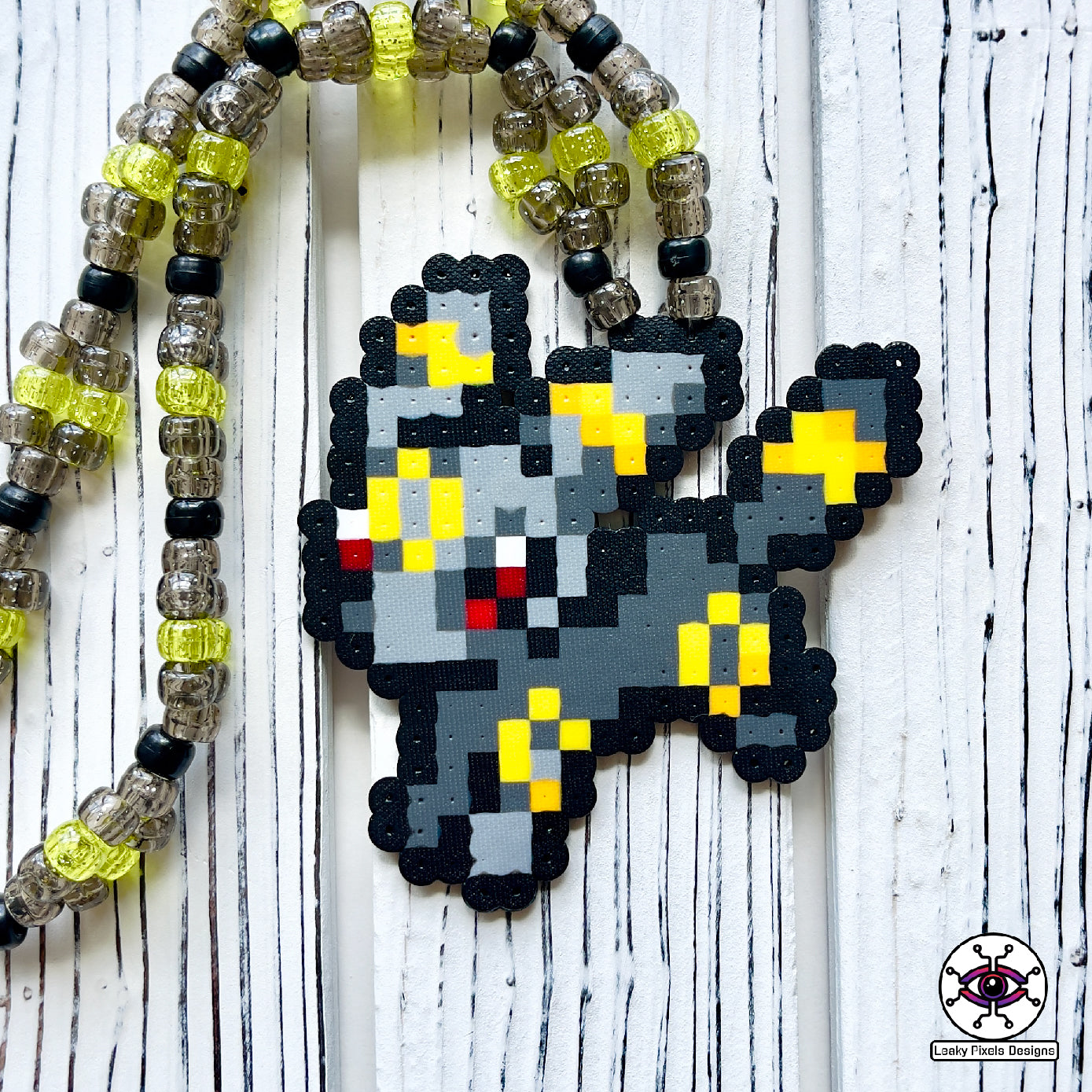 Umbreon pokemon perler necklace. eevee evolution. dark grey with red eyes and gold rings on its body. necklace is made of clear, black, and yellow glitter pony beads.